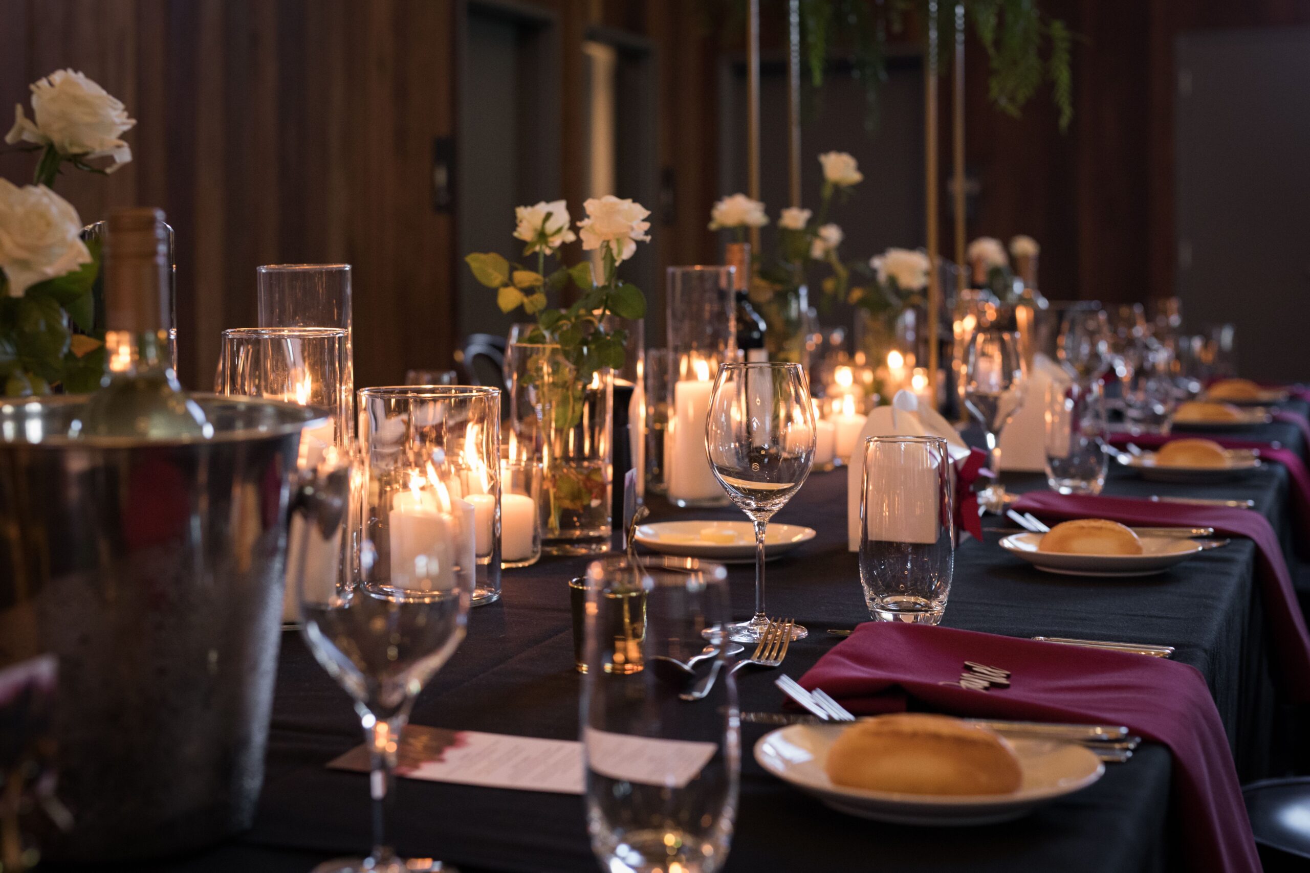 A decorated view of the table setting with candles, white roses, glasses, and a bottle of wine in a bucket