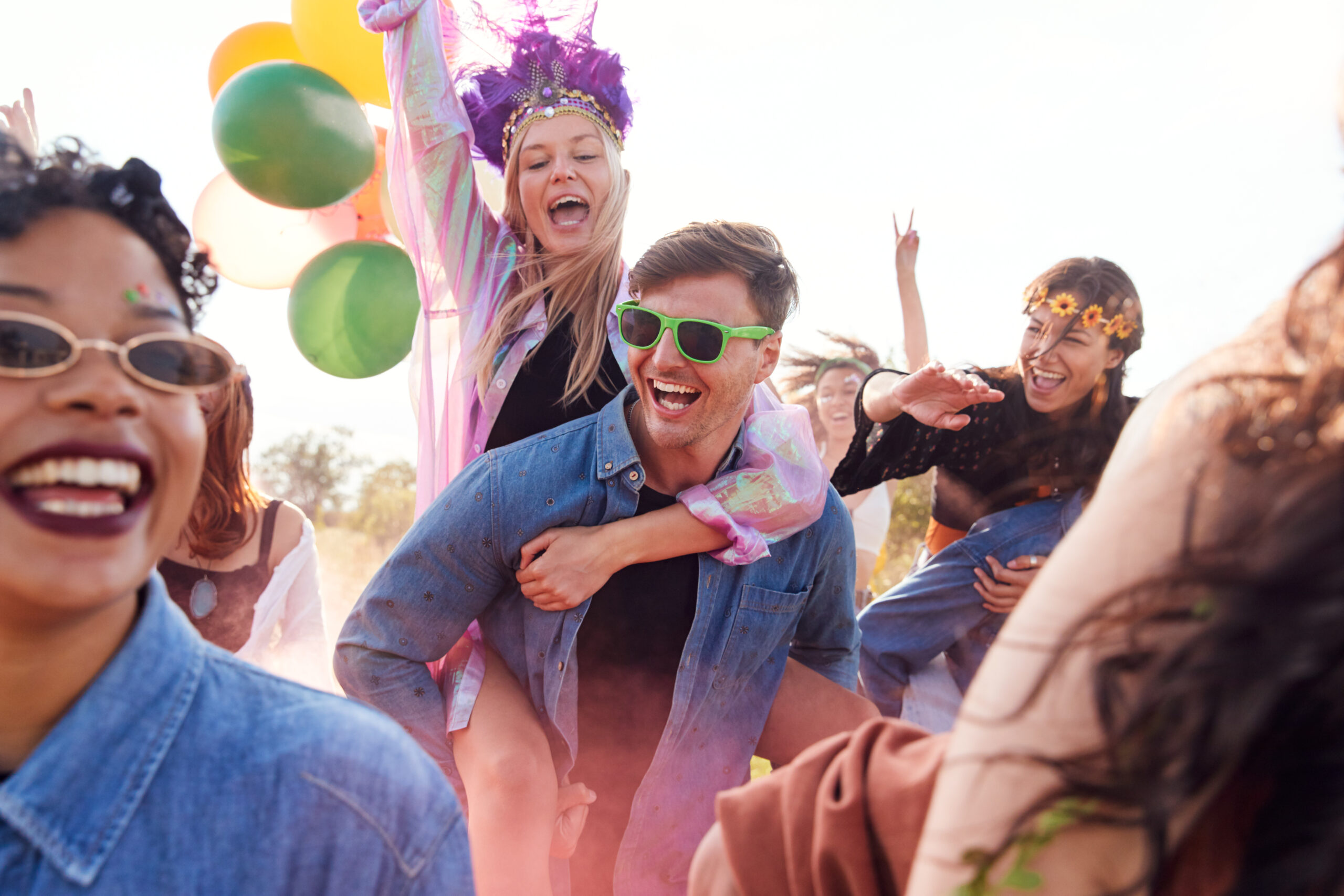 Group Of Friends Walking Back To Tent After Outdoor Music Festival With Balloons And Smoke Flare